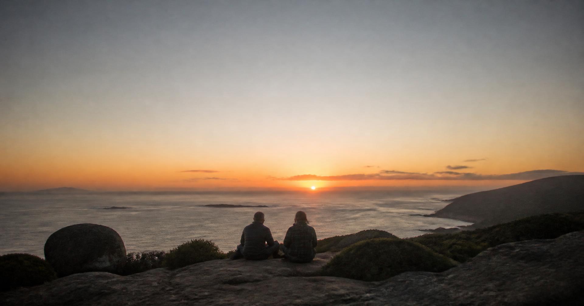 Two travellers watching the sun set from a coastal headland