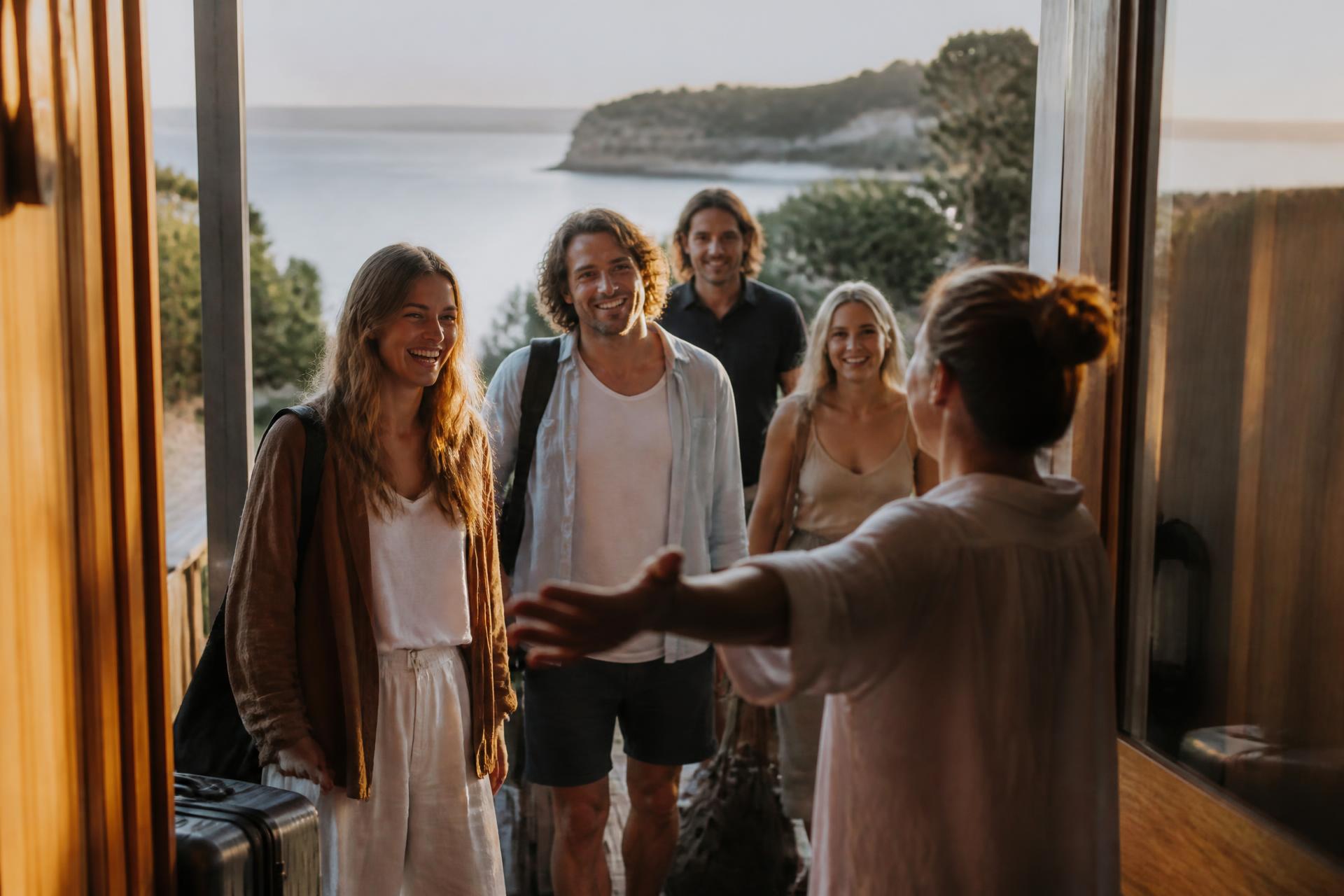 Guests warmly greeted at the door of a coastal holiday home at golden hour.