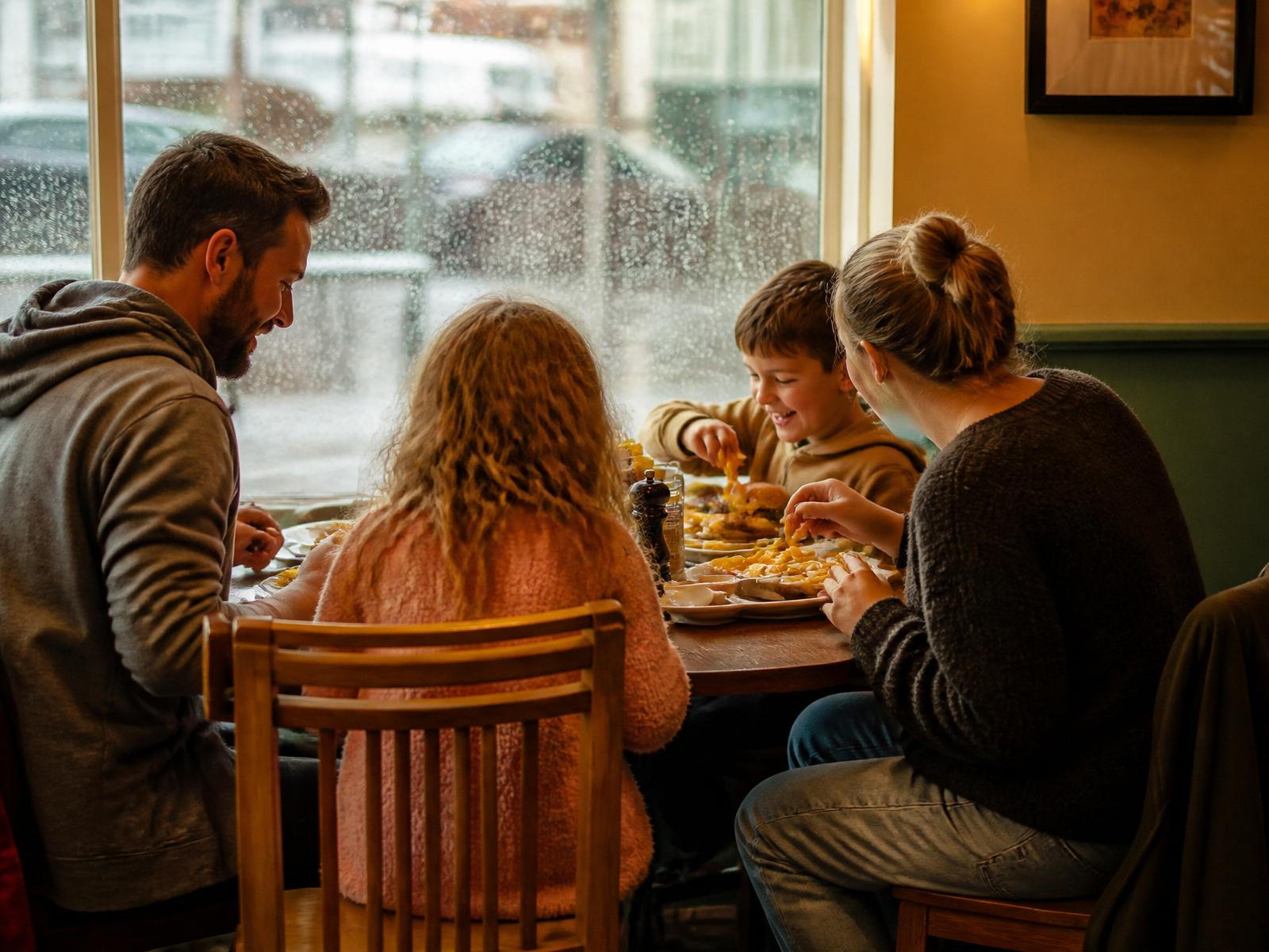 A young family sharing lunch at a regional café while rain runs down the window outside