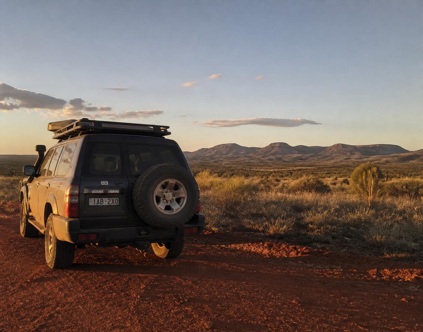 A dusty four-wheel drive parked on a red-dirt track at golden hour