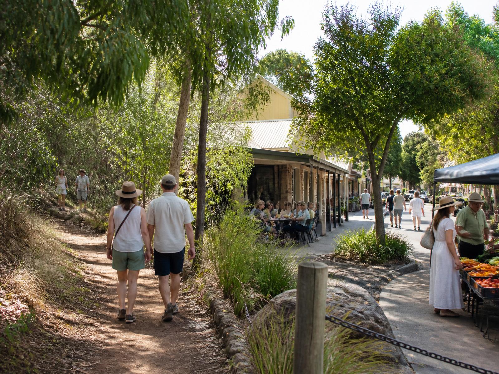 Visitors exploring beyond the main attraction, walking a shaded trail beside a regional street with cafes and a produce stall